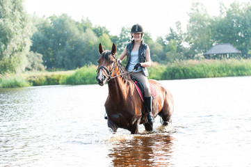 Cheerful young teenage girl riding horseback in river at morning