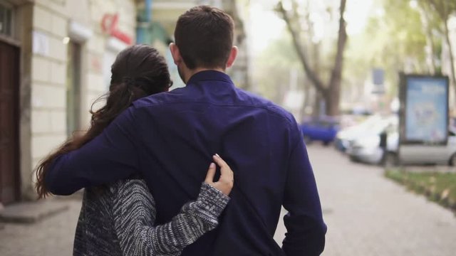 Close-up back view of young beautiful couple walking in the street embracing each other and talking. Romantic date