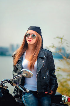 woman in a leather jacket  white shirt and blue jeans in a glasses on a motorcycle on a urban autumn