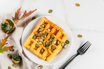 Fototapeta na wymiar Homemade Pumpkin Waffles with maple syrup and pumpkin seeds, on white marble table, copy space top view
