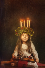 Little caucasian girl in Saint Lucia costume with crown of candles and traditional swedish sweet
