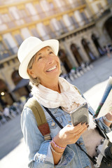 Senior woman visiting Spanish city, using smartphone and map