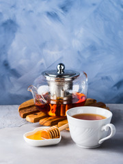 Cup of red tea rooibos and honey with glass teapot on blue