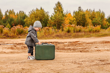 cute little boy opens an old green suitcase in retro clothes