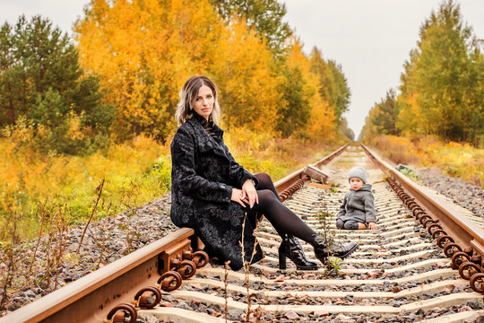 young beautiful woman sitting on the tracks in the woods with the boy and suitcases on background