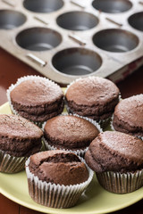 Fresh baked chocolate cup cakes on the plate with baking tray in the background