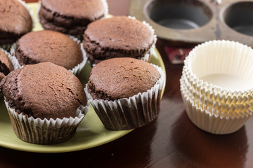 Fresh baked chocolate cup cakes on the plate with baking tray in the background