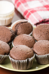 Fresh baked chocolate cup cakes served on the plate with kitchen dishtowel in the background