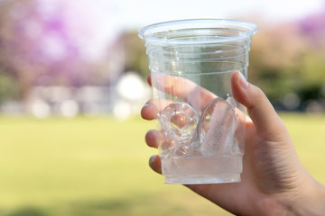 The hands of women holding ice in a glass of water.