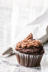 Chocolate cup cake with ganache chocolate cream and piping bag in the background