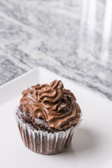 Chocolate cup cake with chocolate ganache cream on the white plate above grey granite background
