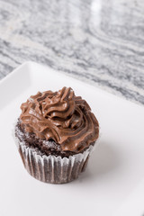 Chocolate cup cake with chocolate ganache cream on the white plate above grey granite background