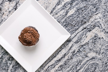 Flat lay above chocolate cup cake on the white square plate above grey granite background