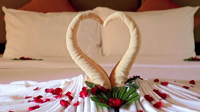 Red rose petals fall on decoration of love from towel on clean bed in a hotel room.