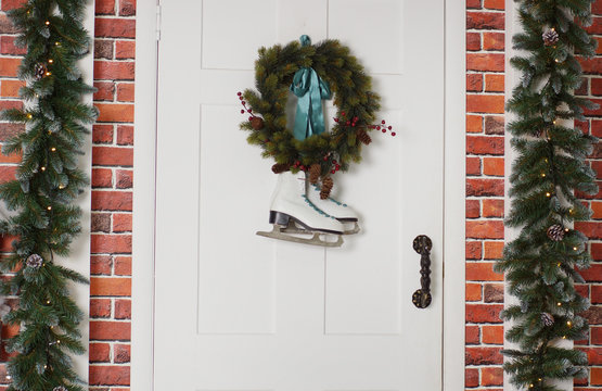 White skates hang with a spruce wreath. Christmas decoration of the front door of the house.