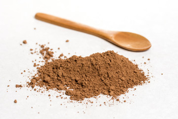 Brown cocoa powder with wooden spoon isolated above white marble background