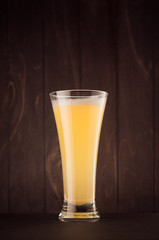Pilsner beer glass with muddy weizen on dark wood board, vertical. Template for advertising, design, branding identity, restaurant menu, cover.
