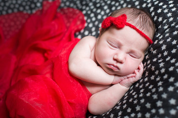 Sleeping pretty newborn in red dress and a small ribbon on his head.