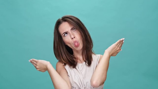 Happy brunette woman in t-shirt covering her face and showing grimaces after that over turquoise background