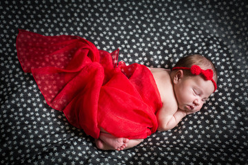 Sleeping pretty newborn in red dress and a small ribbon on his head.