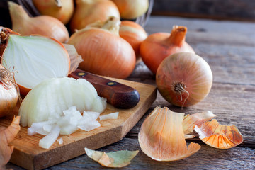 Finely chopped onions next to whole bulbs and husks on a wooden table, horizontal