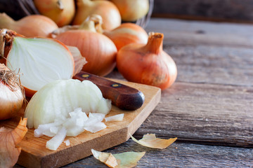 Finely chopped onions next to whole bulbs and husks on a wooden table, horizontal