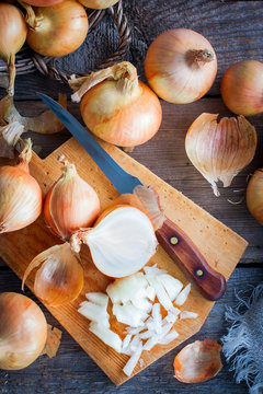 A large onion crop in a wicker basket. Onions are rich in vitamins, useful in spring. Onion peeled against a wooden background. Top view, selective focus