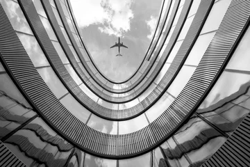 Fliegendes Flugzeug und modernes Architekturgebäude, abstrakt aussehendes Schwarz-Weiß-Bild mit niedrigem Winkel © BOOCYS