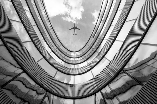 Flying airplane and modern architecture building, low angle black and white abstract looking picture © BOOCYS