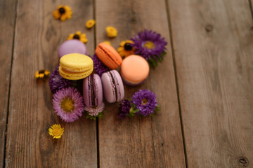 Obraz na płótnie Canvas Violet and yellow macarons and flowers on wooden table background. Colorful french dessert with fresh flowers. Autumn concept