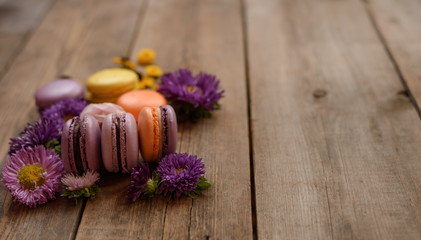 Violet and yellow macarons and flowers on wooden table background. Colorful french dessert with fresh flowers. Autumn concept