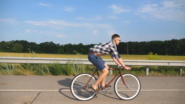 Young handsome man riding at vintage bicycle in the country road. Sporty guy cycling at the track. Male cyclist riding fixed gear bike at highway. Healthy active lifestyle Slow motion