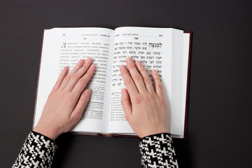 Jewish book, with woman's hand, on black background. Text of the Hebrew, prayer. Woman prays with book. © ksana_uk