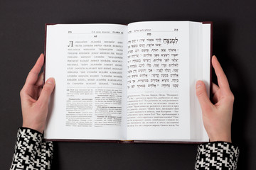 Jewish book, with woman's hand, on black background. Text of the Hebrew, prayer. Woman reading book.