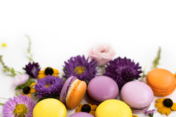 Macarons and flowers wreath on a white background. Colorful french dessert with fresh flowers. Top view