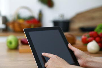 Close-up of human hands are gesticulate over a tablet in the kitchen. Women choosing menu or making...