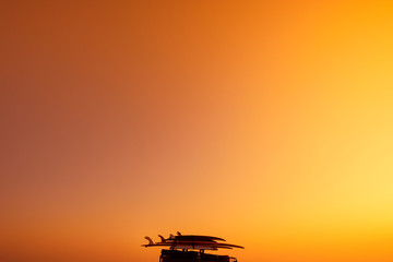 Fototapeta na wymiar Surf boards and luggage on the roof of the van at warm summer sunset light with sky as copy space