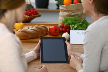 Close-up of four human hands are gesticulate over a tablet in the kitchen. Friends having fun while choosing menu or making online shopping. So much ideas for tasty cooking. 