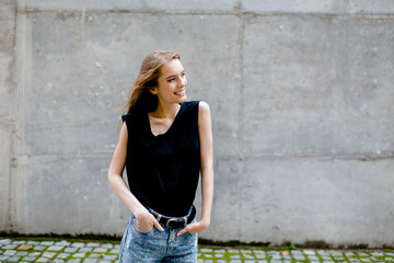 View of pretty young female standing in the street against grey wall Natural beauty, woman in casual clothes looking aside.