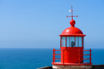 Red lighthouse roof cupola lantern room with a wind vane over clear blue summer sky background with copy space