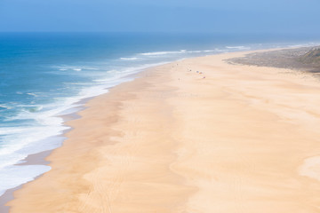 Aerial view of people sunbathing and playing on the wide empty endless sandy ocean beach at hot summer day