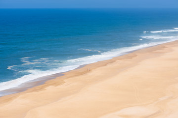 Aeria view of wide empty sandy beach with deep blue ocean clear sky and two people standing on the shore in Portugal