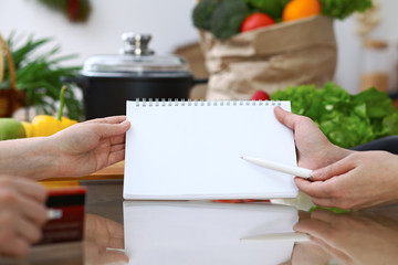 Close-up of human hands pointing into note book copy space area in the kitchen. So much ideas for tasty cooking. Vegetarian, healthy meal and friendship concept