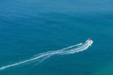 Naklejka premium Tourists taking ride by speed boat on rubber tube boat on waves in ocean, aerial view