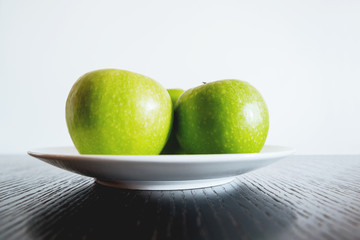 Three fresh green apples on white plate.