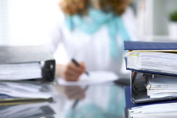 Binders with papers are waiting to be processed with businesswoman or secretary back in blur....