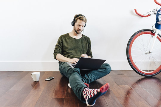 Man with headphones sitting on the floor at home using laptop