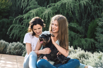 Beautiful mother with teenage daughters and pet zwergschnauzer dog sitting in garden near home