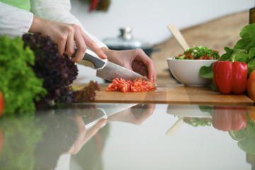 Closeup of human hands cooking vegetables salad in kitchen on the glass  table with reflection