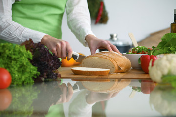 Closeup of human hands cooking in kitchen on the glass table with reflection. Housewife slicing bread
